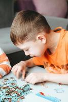 garçon dans un t-shirt orange recueille un puzzle sur la table. temps sans gadgets. jeux de société pour enfants. le garçon développe la motricité fine et le cerveau photo