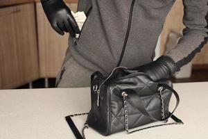 voleur en tenue noire et gants voir dans le sac ouvert des femmes volées. le voleur sort l'or et l'argent d'un sac à main de femme dans la cuisine photo