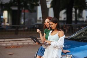 deux jeunes femmes avec un ordinateur portable près de la voiture photo