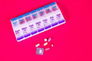 Boîte à pilules hebdomadaire contenant sur fond rouge lisse photo