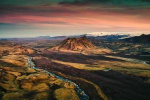 cratère volcanique éteint parmi le champ de lave et la rivière qui coule au coucher du soleil dans les hautes terres islandaises en été photo