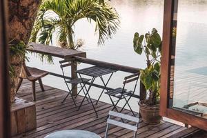 table et chaises en bois vides sur patio dans un jardin tropical au bord du lac