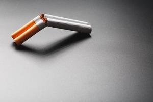 deux cigarettes sous la forme d'un fusil de chasse à double canon sur fond noir avec espace de copie. arrêter de fumer. le concept de fumer tue. photo