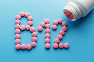 Pilules rondes roses en forme de vitamines b12 sur fond bleu renversées d'une boîte blanche photo