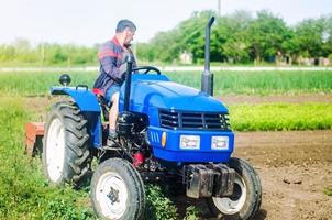 un agriculteur conduit un tracteur tout en travaillant sur un champ agricole. ameublir la surface, cultiver la terre. l'élevage, l'agriculture. utilisation de machines et d'équipements agricoles pour simplifier et accélérer le travail. photo