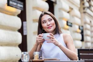 belle jeune femme asiatique avec une tasse de café. femme aime le café frais le matin avec le lever du soleil au café belle femme buvant du café le matin assis à l'extérieur photo