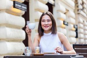 belle jeune femme asiatique avec une tasse de café. femme aime le café frais le matin avec le lever du soleil au café belle femme buvant du café le matin assis à l'extérieur photo