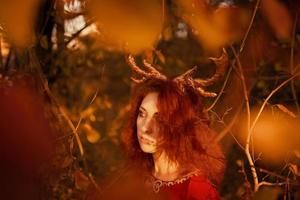 femme en longue robe rouge avec des cornes de cerf dans la forêt d'automne. photo