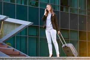 femme d'affaires partant en voyage d'affaires portant des valises tout en parlant sur son téléphone portable. femme d'affaires à l'aéroport international se déplaçant à la porte du terminal pour un voyage en avion photo