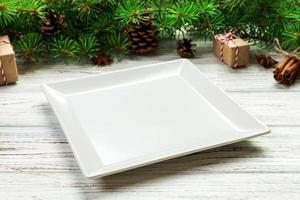 vue de perspective. assiette carrée blanche vide sur fond de noël en bois. concept de plat de dîner de vacances avec un décor de nouvel an photo