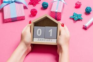 vue de dessus des mains féminines tenant le calendrier sur fond rose. le premier janvier. décorations de vacances. notion de nouvel an photo