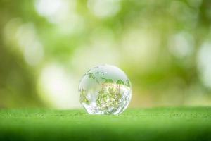 gros plan sur un globe de cristal reposant sur l'herbe dans une forêt - concept d'environnement. environnement, social et gouvernance dans les affaires durables et éthiques sur fond vert. photo