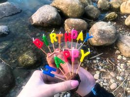 inscription de joyeux anniversaire faite de bougies de vacances entre les mains d'un homme et d'une femme en face de l'eau de la rivière du lac océanique photo