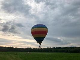 Grand ballon volant multicolore à rayures rondes et lumineuses de couleur arc-en-ciel avec un panier contre le ciel le soir photo