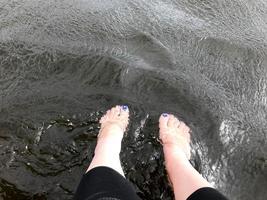 de beaux pieds féminins des pieds avec des doigts avec une manucure de mode multicolore sont tombés suspendus dans de l'eau noire sombre et froide photo