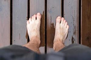 pieds nus pieds masculins se tiennent sur un sol en bois humide, après la pluie, en plein air. photo