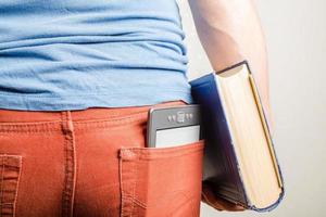 e-book est dans la poche arrière du jean homme, et à la main il tient un vieux livre en papier épais. notion d'éducation. comparaison. photo