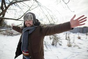 un homme heureux et souriant étend les bras sur les côtés et regarde dans la caméra, il est heureux de marcher dans un parc enneigé, un jour de printemps. photo