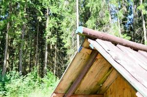 toit triangulaire en pente d'une petite maison de hutte délabrée en bois dans une forêt de grumes de planches sur fond d'arbres photo