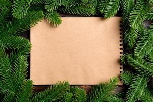 vue de dessus du cahier en papier kraft décoré d'un cadre en sapin sur fond en bois. concept de temps du nouvel an photo