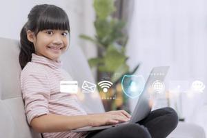 sécurité des enfants en ligne. petite fille utilisant un ordinateur portable à la maison. icône de l'application de blocage d'internet au premier plan photo