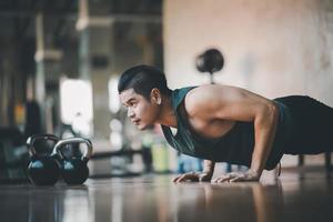 sportif asiatique en forme faisant des exercices de poussée sur le plancher de bois à la salle de gym fitness. exercice d'homme de sport au centre sportif. concept de salle de sport de remise en forme. photo