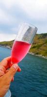 main d'homme tenant un verre de vin rouge avec fond de mer, montagne et ciel. célébrer et faire la fête entre la nature et les voyages. photo