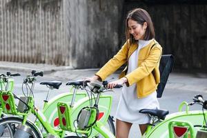 vélo de ville - femme asiatique utilisant le système de partage de vélos publics de la ville. faire du vélo des vélos de ville de stationnement professionnels féminins après avoir fait du vélo sur un vélo de ville. photo