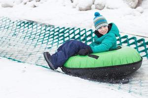 enfant s'amusant sur le tube de neige. garçon monte un tube. animations hivernales. enfant glissant en descente sur tube photo