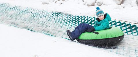 enfant s'amusant sur le tube de neige. garçon monte un tube. animations hivernales. enfant glissant en descente sur tube. bannière photo