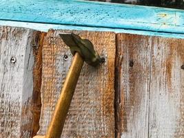 marteau sur un manche en bois avec une extrémité en métal. clous de marteau sur une surface en bois. des clous métalliques sont enfoncés dans une planche peinte en bleu. construction de clôture photo