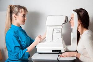 femme ophtalmologiste dans la salle d'examen avec une jeune belle brune assise sur une chaise regardant dans la machine de test oculaire photo