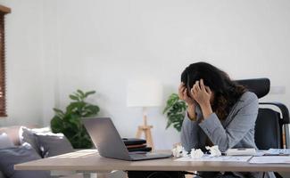 une femme d'affaires fatiguée et stressée travaille sur un ordinateur portable tout en étant assise à une table à la maison et tient sa main sur ses tempes, crise de migraine. freelance, travail à domicile.