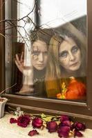 deux femmes sorcières regardent à travers une toile d'araignée sinistrement par la fenêtre sur fond de décorations d'halloween. mascarade, fête d'halloween photo