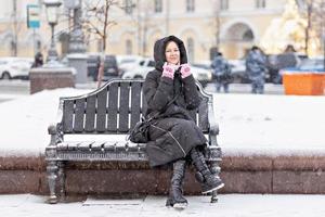 une jeune femme chaudement vêtue est assise sur un banc dans la ville dans la rue par une journée froide et enneigée photo