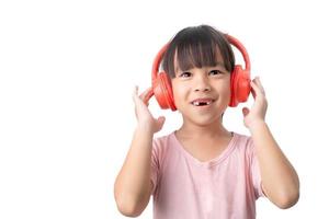 heureuse petite fille asiatique souriante écoutant de la musique sur un casque sans fil isolé sur fond blanc. photo