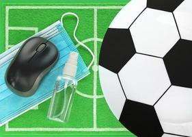 souris d'ordinateur, désinfectant, masque médical bleu, assiette vide comme un ballon de football placé sur un mini terrain de football en feutre vert, vue de dessus. concept restez à la maison pendant le coronavirus et regardez le match diffusé en ligne. photo