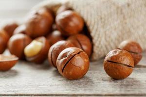 noix de macadamia renversées hors du sac sur un fond en bois gros plan avec une noix pelée photo