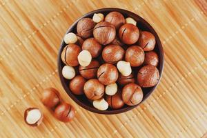 noix de macadamia sur texture de bambou dans une tasse en bois, noix pelée et non pelée, vue de dessus photo