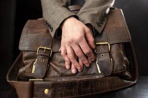 les mains des enseignants sont sur une vieille mallette en cuir avec des boucles en métal sur la table. photo