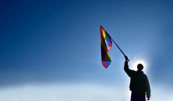 drapeau arc-en-ciel tenant à la main sur fond de ciel bleu, concept pour la célébration lgbt du mois de la fierté, juin, dans le monde entier. photo