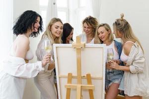 groupe de femmes peignant sur toile et buvant du vin blanc pendant la fête à la maison photo