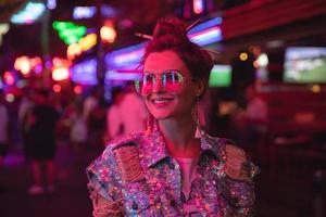 femme élégante portant une veste avec des paillettes brillantes dans la rue de la ville avec des néons