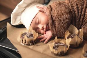 nouveau-né portant une toque de chef est allongé sur le plateau du four avec des muffins photo