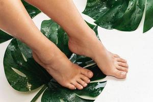 pieds féminins humides avec une peau lisse et des feuilles tropicales de monstera deliciosa photo