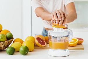 mains féminines et presse-agrumes pendant la préparation du jus d'orange frais photo