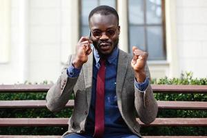 African American man parle sur le smartphone assis sur le banc à l'extérieur photo