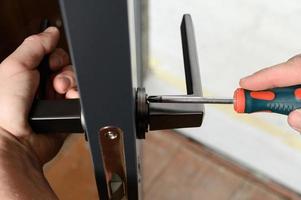 un homme installe une poignée de porte dans une porte, menuiserie à la maison. photo