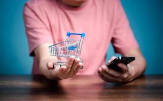 shopping en ligne avec panier, homme utilisant un téléphone portable acheter des choses sur la boutique de la page web. photo
