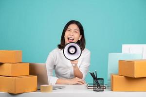 femme d'affaires asiatique assise à son bureau avec ordinateur portable et carton marron isolé sur fond vert pastel. elle criait et criait avec un mégaphone à la main. photo